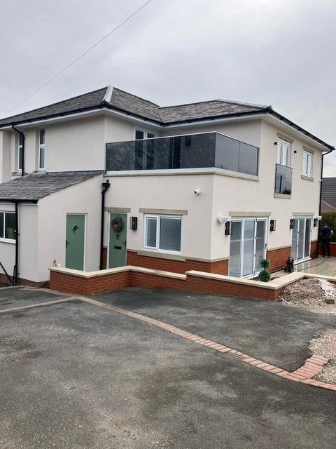 Finished extension from the driveway: cream render, glass balcony, bi-fold doors and green front doors